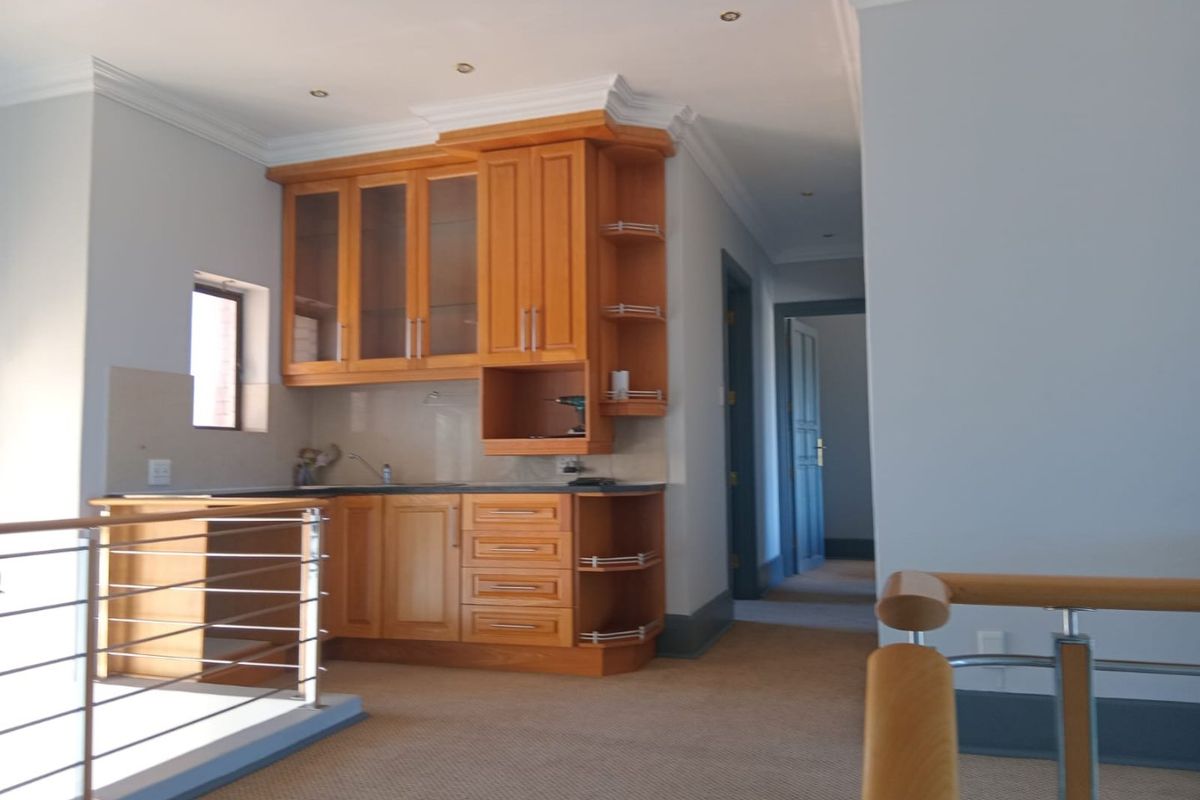 A compact kitchen area featuring wooden cabinetry and built-in shelving, situated adjacent to a staircase with a modern wood and steel railing.