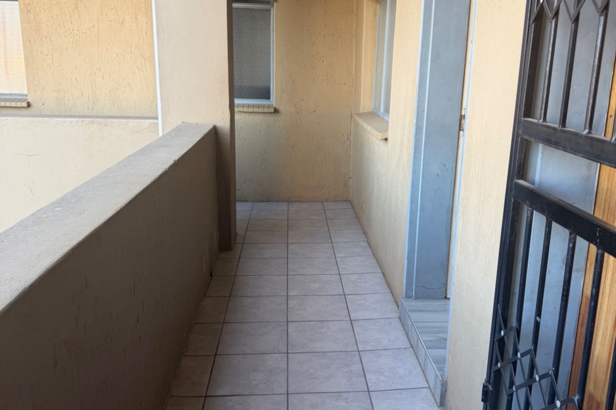 A functional apartment balcony featuring tiled flooring, a concrete balustrade, and a secure metal gate entrance.