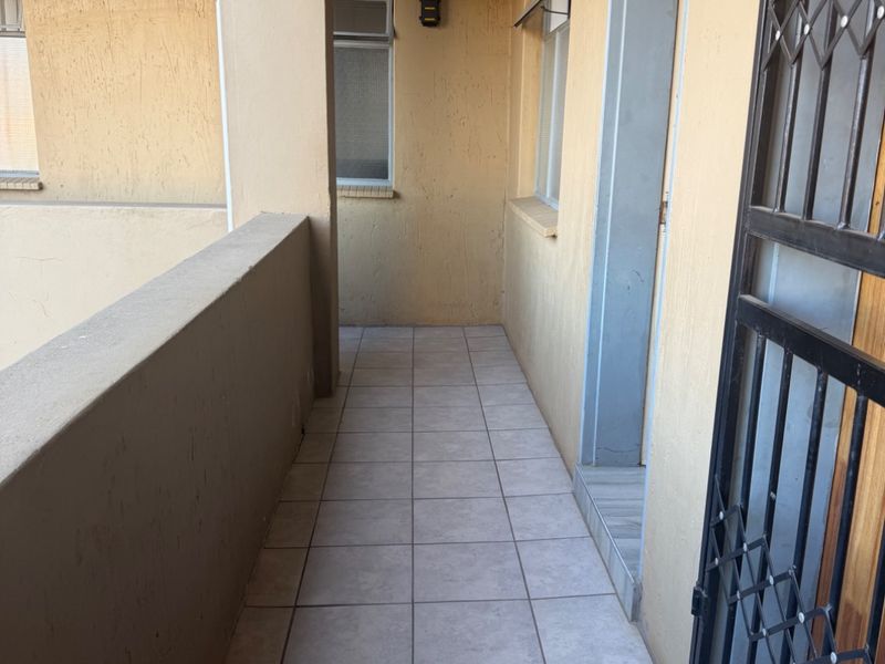 A functional apartment balcony featuring tiled flooring, a concrete balustrade, and a secure metal gate entrance.