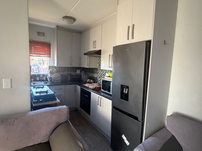 Compact open-plan kitchen featuring white cabinetry, tiled backsplash, built-in oven, extractor fan, and laminate flooring, seamlessly integrated with the living area.