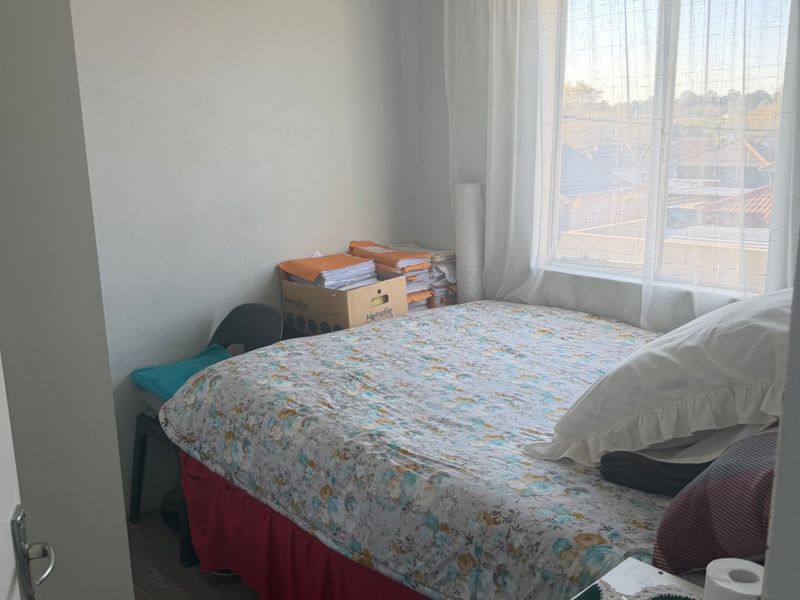 A compact bedroom featuring laminate flooring and a large window providing natural light and neighborhood views.