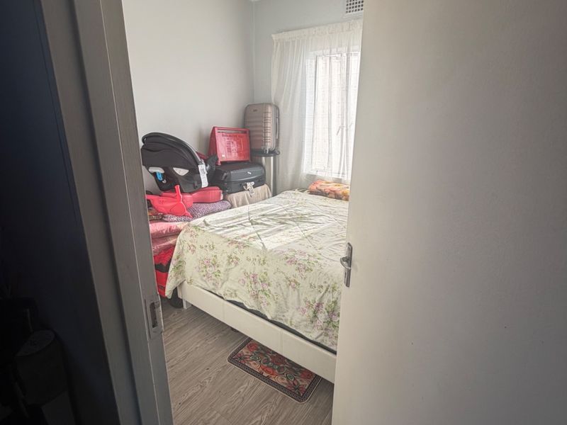 A compact bedroom featuring laminate flooring, a central ceiling light, and a window with curtains, viewed from the doorway.