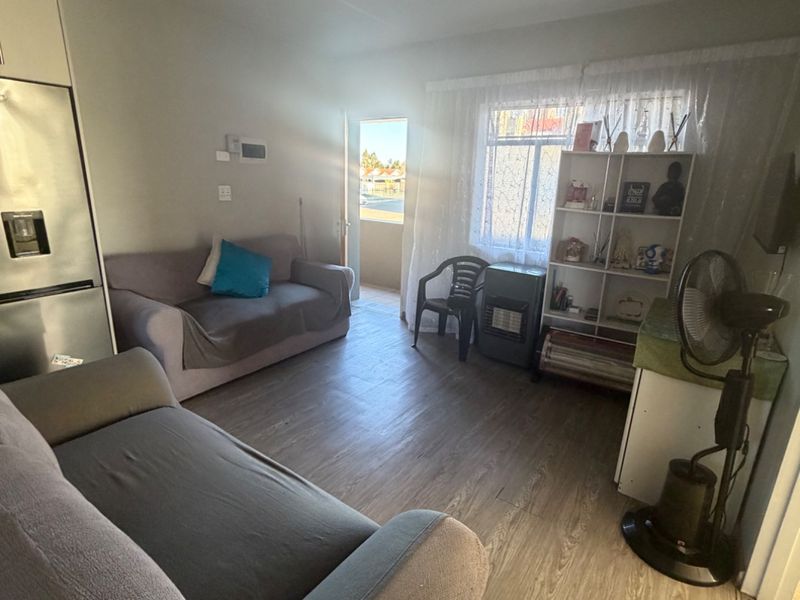A living room area featuring laminate flooring and natural light from the adjacent balcony entrance.