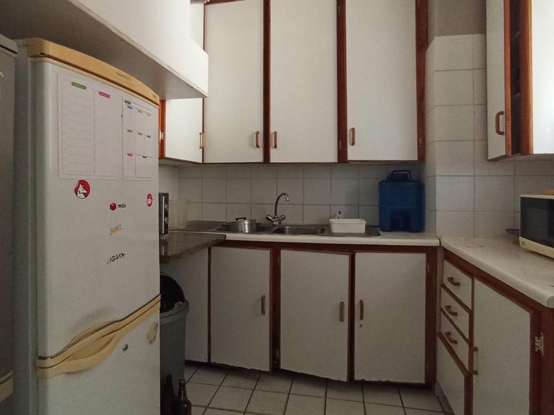 A functional kitchen featuring white cabinetry with wood trim, tiled backsplash, and tiled flooring, offering a dated aesthetic ready for modernization.