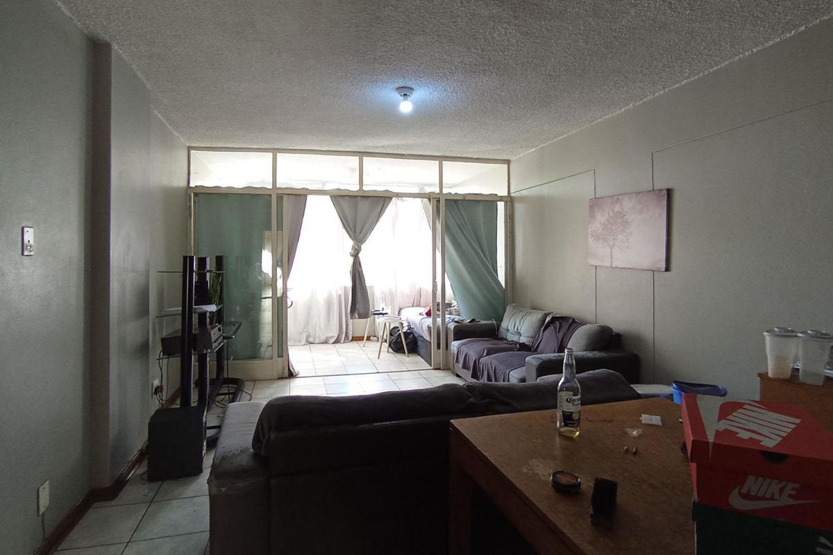 A living room area featuring tiled flooring and a glass partition leading to an enclosed balcony, requiring cosmetic updates to improve the overall aesthetic.