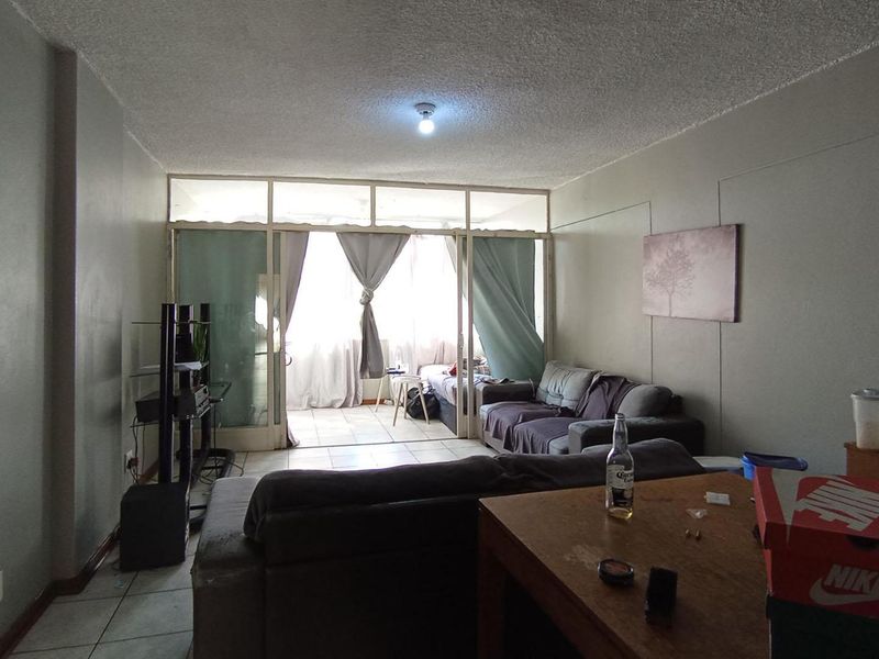 A living room area featuring tiled flooring and a glass partition leading to an enclosed balcony, requiring cosmetic updates to improve the overall aesthetic.
