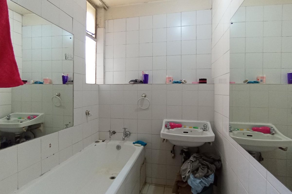 A dated bathroom featuring a standard bathtub, wall-mounted basin, and extensive wall tiling, requiring cosmetic updates to improve its overall condition and appeal.