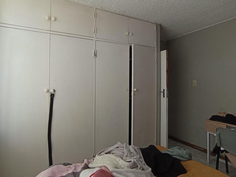 A bedroom featuring floor-to-ceiling built-in cupboards and a textured ceiling, offering potential for modernization and improved storage aesthetics.