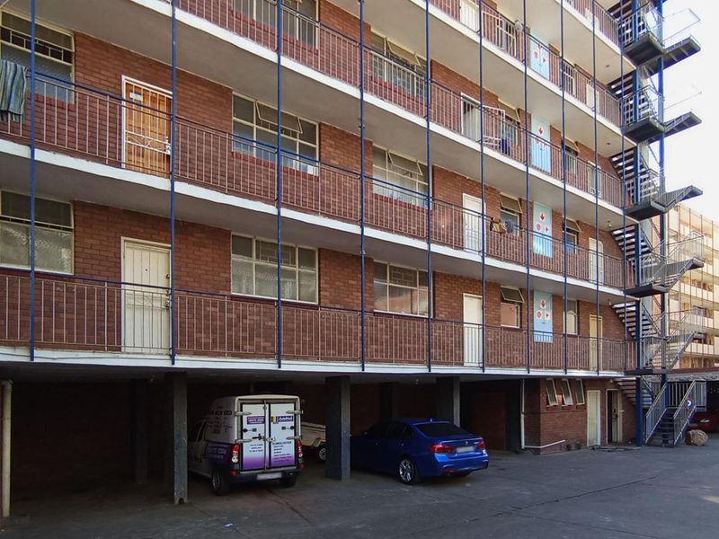 Exterior view of a multi-story apartment building featuring brick facade, external steel staircases, and a ground-level covered parking area.