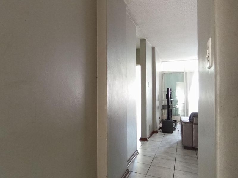 A narrow hallway with tiled flooring leading towards a bright living area with a sliding glass door.