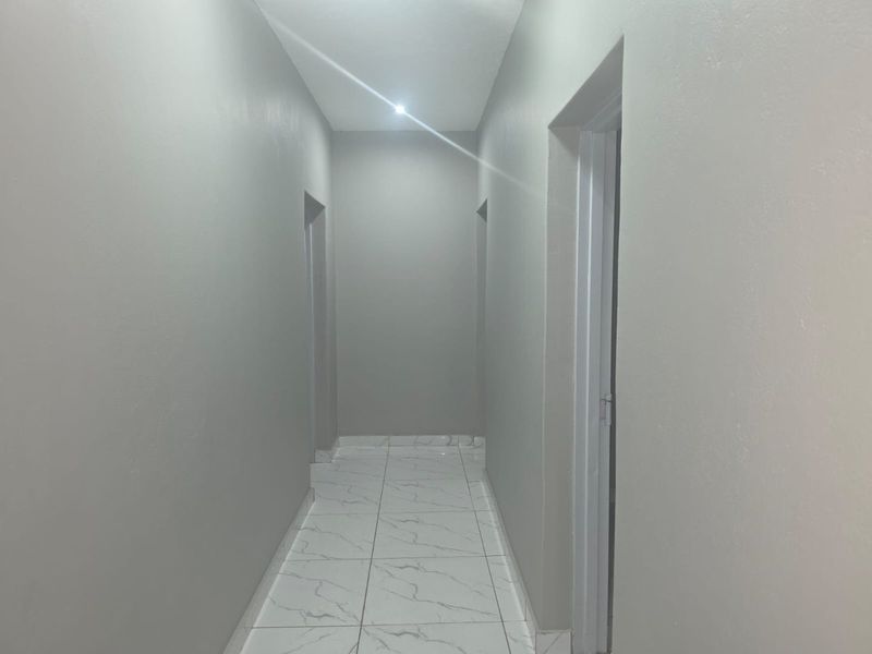 A clean, minimalist hallway featuring neutral grey walls and modern marble-look floor tiles with recessed ceiling lighting.