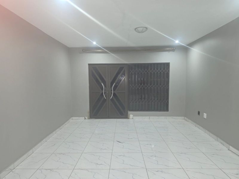 An empty, well-lit living room featuring modern white marble-look floor tiles, neutral grey walls, and a secure entrance door with a security gate.