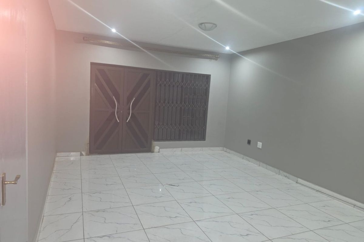 A spacious, empty living area featuring modern white marble-look floor tiles, recessed downlighting, and a secure double-door entrance with integrated security gate.