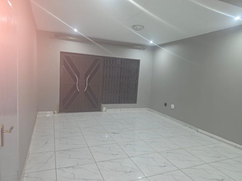 A spacious, empty living area featuring modern white marble-look floor tiles, recessed downlighting, and a secure double-door entrance with integrated security gate.