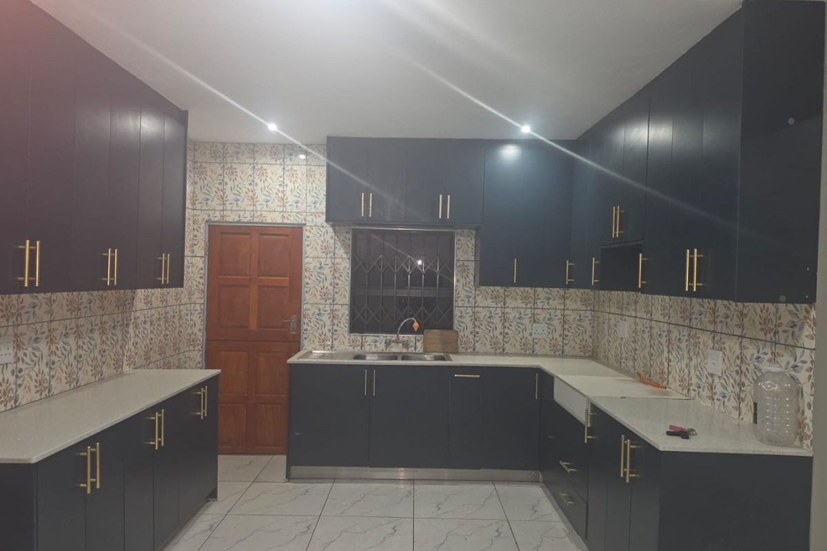 A modern kitchen featuring dark cabinetry, stone countertops, a double basin sink, and decorative tiled backsplash with neutral floor tiles.