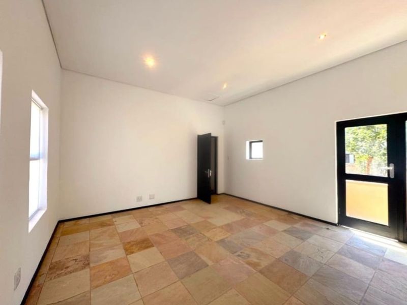 A bright, empty living area featuring natural stone tile flooring, recessed lighting, and direct access to the exterior through a glass-paneled door.