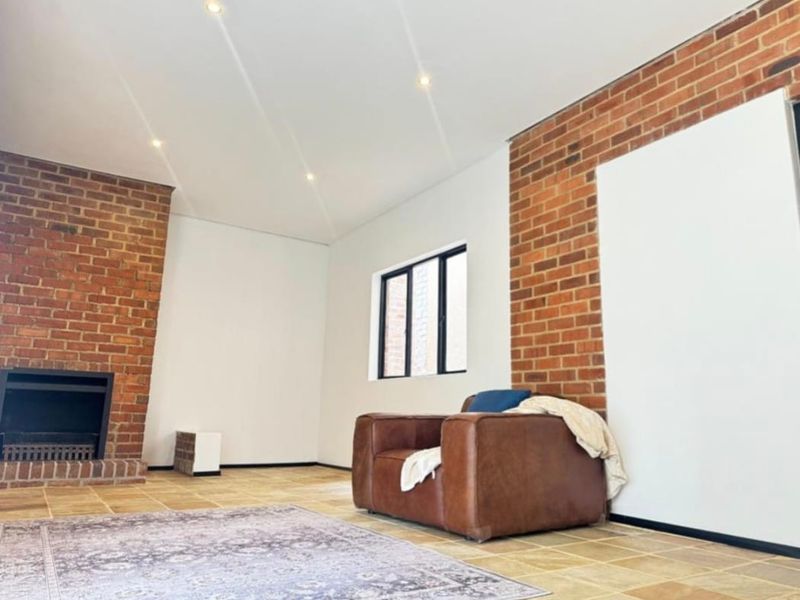 Spacious living room featuring a classic brick fireplace, exposed brick accent walls, tiled flooring, and modern recessed lighting.