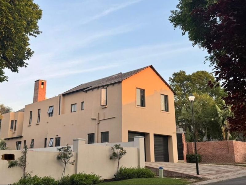 A well-maintained double-story residential property featuring a paved driveway, double garage, and a prominent brick chimney, set behind a secure boundary wall.