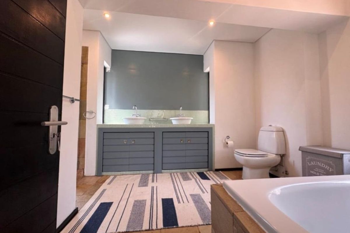 A well-lit bathroom featuring a double vanity with vessel sinks, built-in cabinetry, a toilet, and tiled flooring.