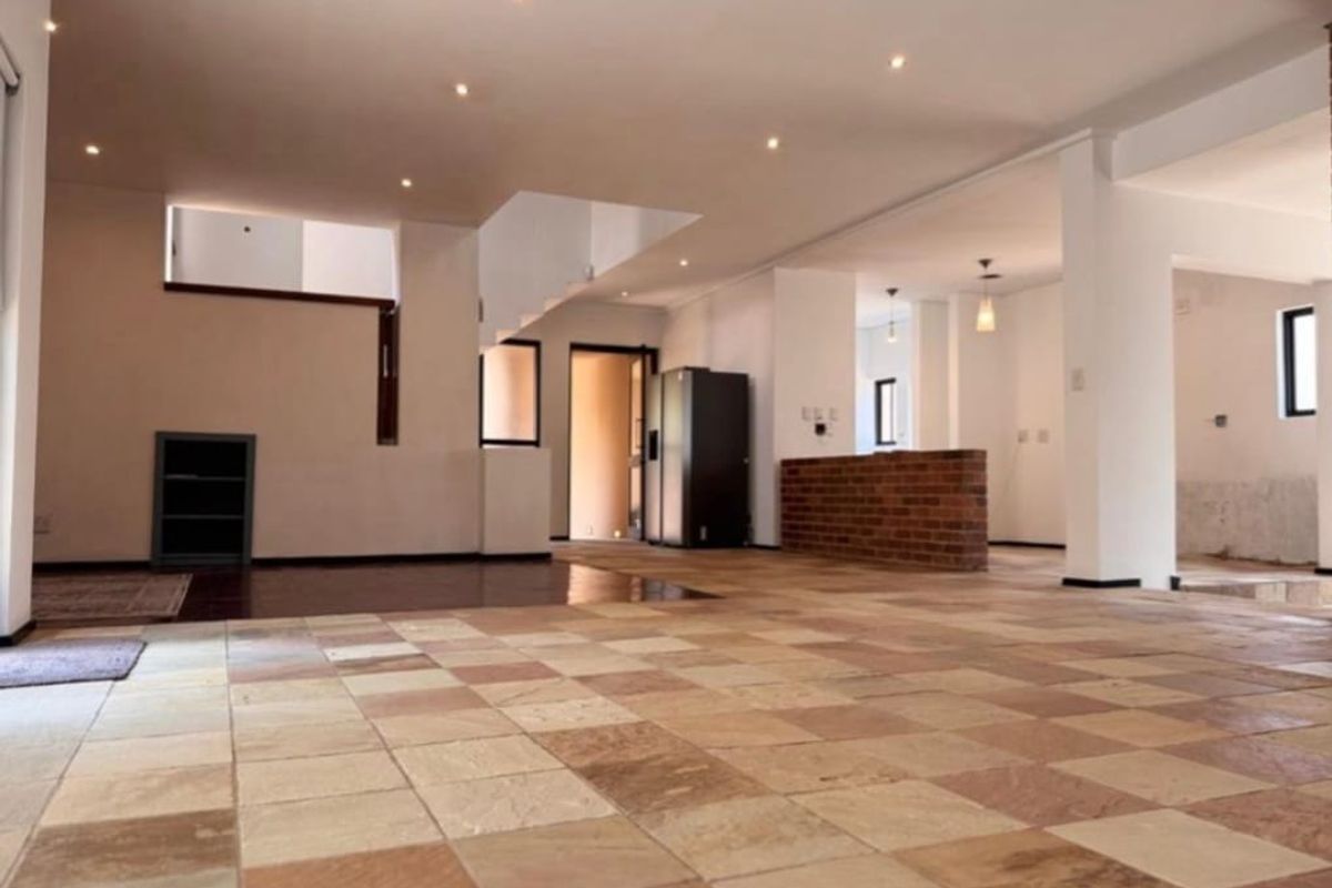 Spacious open-plan living area featuring natural stone tile flooring, recessed lighting, and a brick feature wall, offering a versatile layout for modern living.