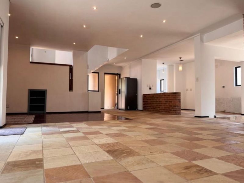 Spacious open-plan living area featuring natural stone tile flooring, recessed lighting, and a brick feature wall, offering a versatile layout for modern living.
