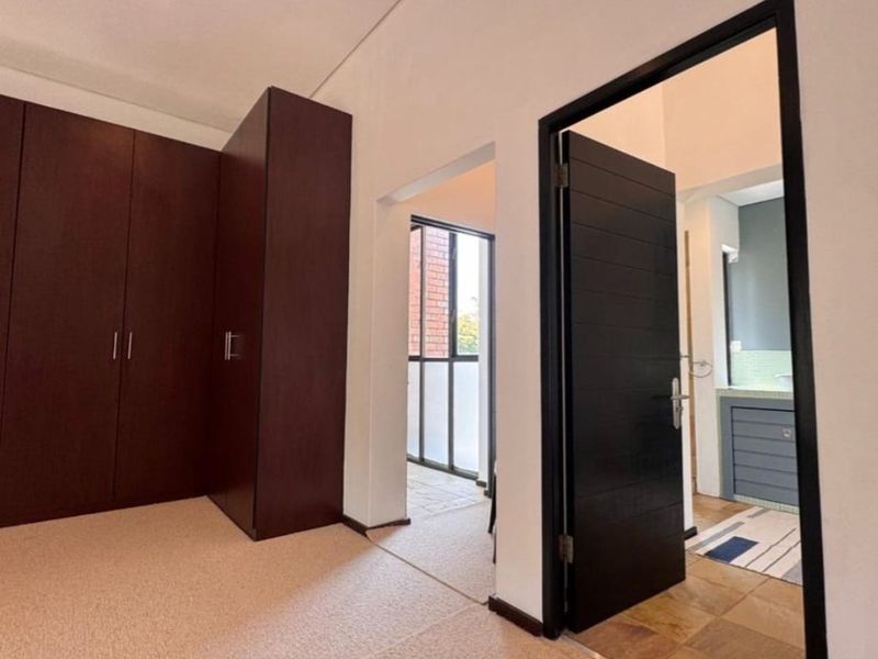 A spacious bedroom featuring built-in dark wood cupboards, carpeted flooring, and direct access to an adjacent bathroom and hallway area.