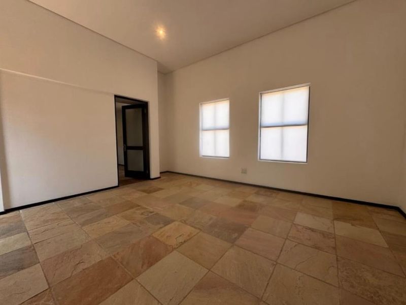 A bright, empty living area featuring natural stone tile flooring, neutral walls, and recessed lighting, offering a clean and versatile space.
