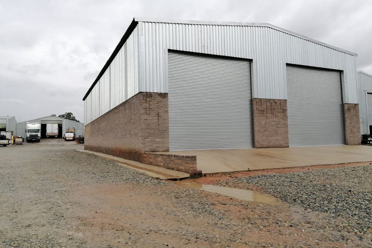 Industrial warehouse facility featuring corrugated metal cladding, brick masonry base, and dual roller shutter doors with a concrete apron.