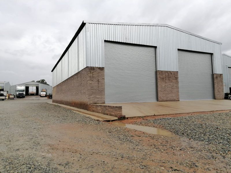 Industrial warehouse facility featuring corrugated metal cladding, brick masonry base, and dual roller shutter doors with a concrete apron.