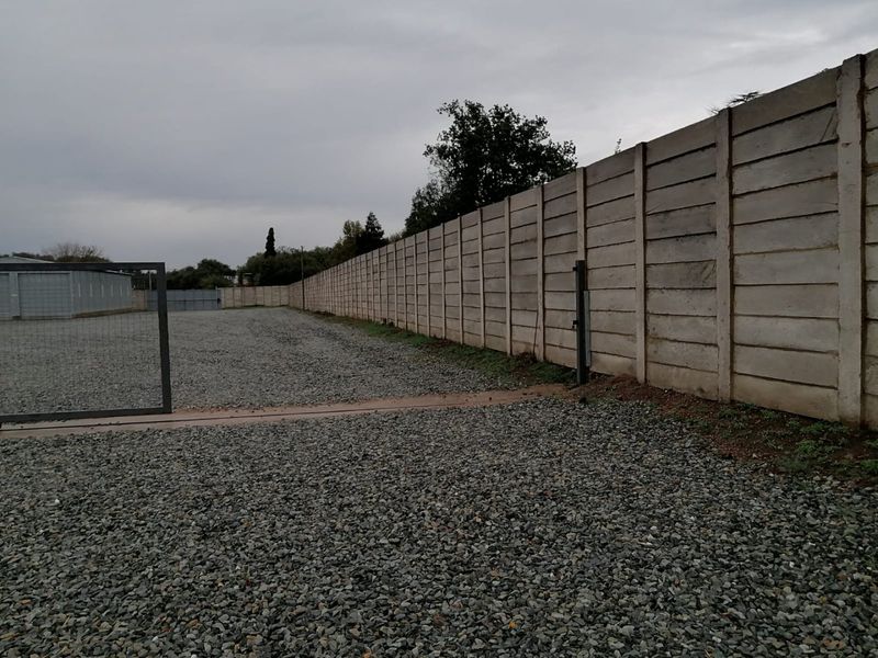 A spacious industrial yard featuring a gravel surface enclosed by a tall precast concrete boundary wall and a secure metal gate.