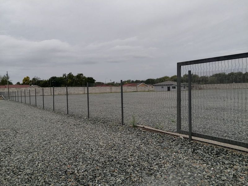 A spacious industrial yard featuring a gravel surface, enclosed by secure mesh perimeter fencing and a precast concrete boundary wall.