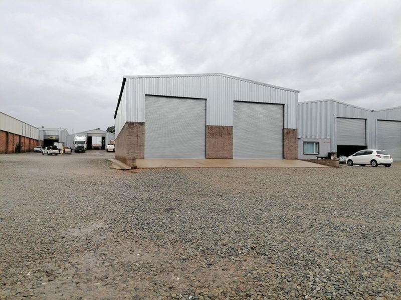 Industrial warehouse facility featuring multiple roller shutter doors, corrugated metal cladding, and a large gravel yard for vehicle access and maneuvering.