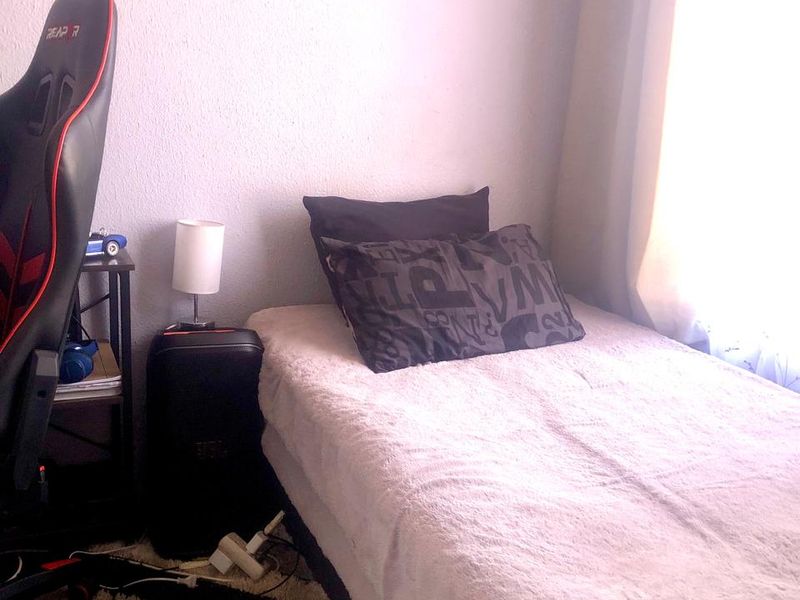 A compact bedroom featuring a single bed positioned against a wall with natural light entering from the side window.