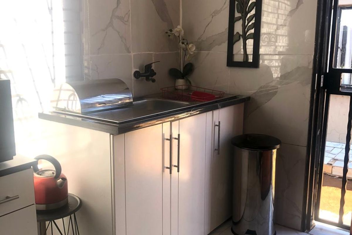 A compact scullery area featuring modern marble-look wall and floor tiles, built-in cabinetry, and a stainless steel sink with direct access to the exterior.