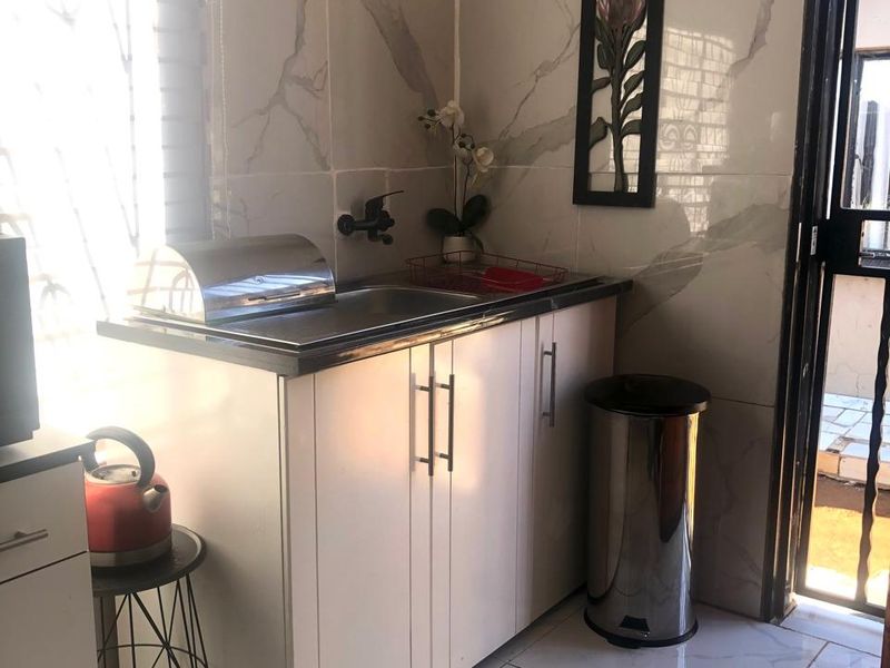 A compact scullery area featuring modern marble-look wall and floor tiles, built-in cabinetry, and a stainless steel sink with direct access to the exterior.