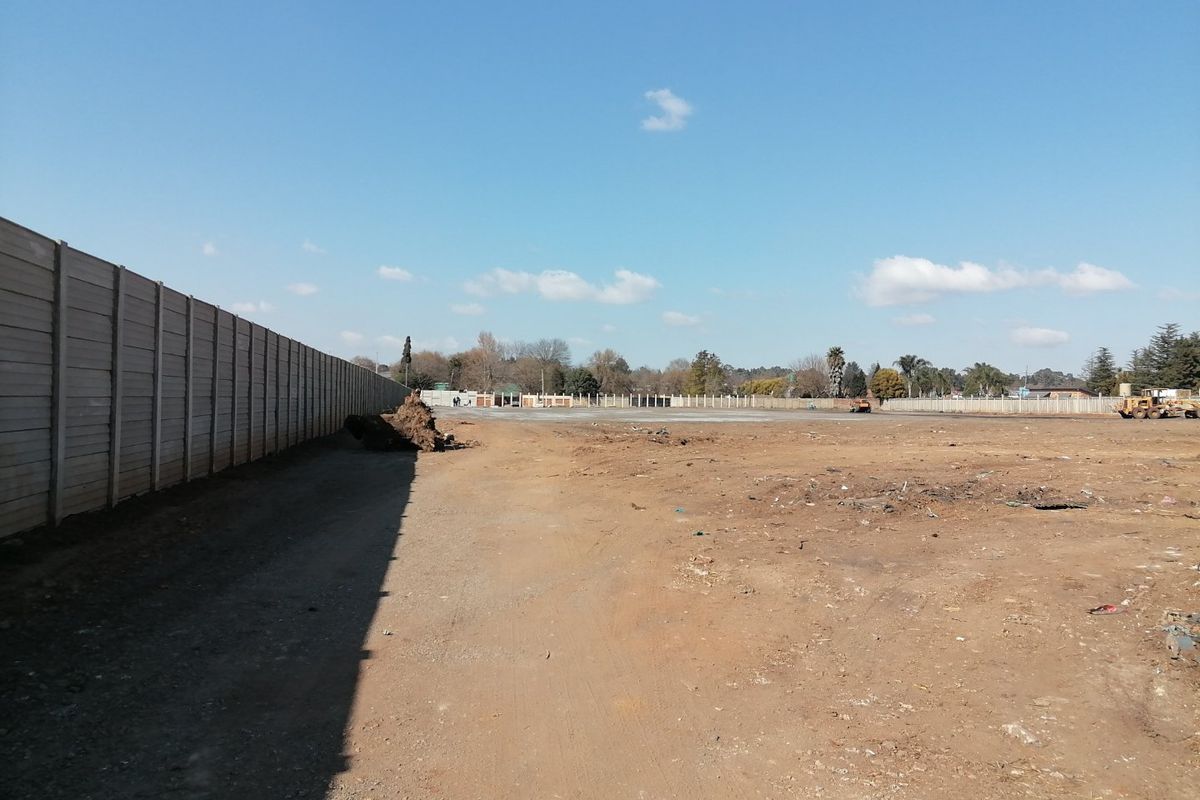 A large, cleared vacant residential plot enclosed by a precast concrete boundary wall, offering a blank canvas for future development.