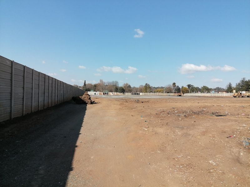 A large, cleared vacant residential plot enclosed by a precast concrete boundary wall, offering a blank canvas for future development.