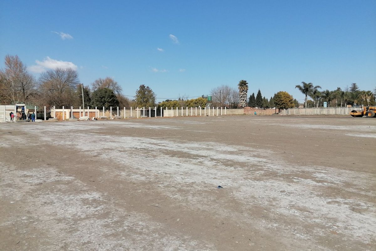 A large, cleared residential plot of land featuring a perimeter precast concrete boundary wall under a clear blue sky.
