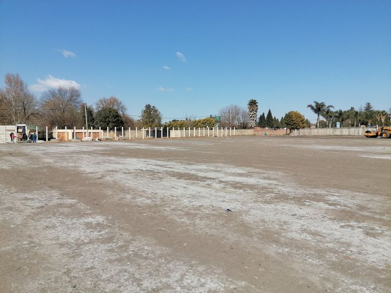 A large, cleared residential plot of land featuring a perimeter precast concrete boundary wall under a clear blue sky.