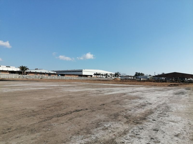 A wide-angle view of a vacant residential land plot featuring cleared ground and perimeter fencing, situated in an industrial-adjacent area.
