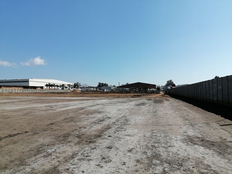 A large, cleared vacant residential plot featuring a precast concrete boundary wall and level ground, ready for development.