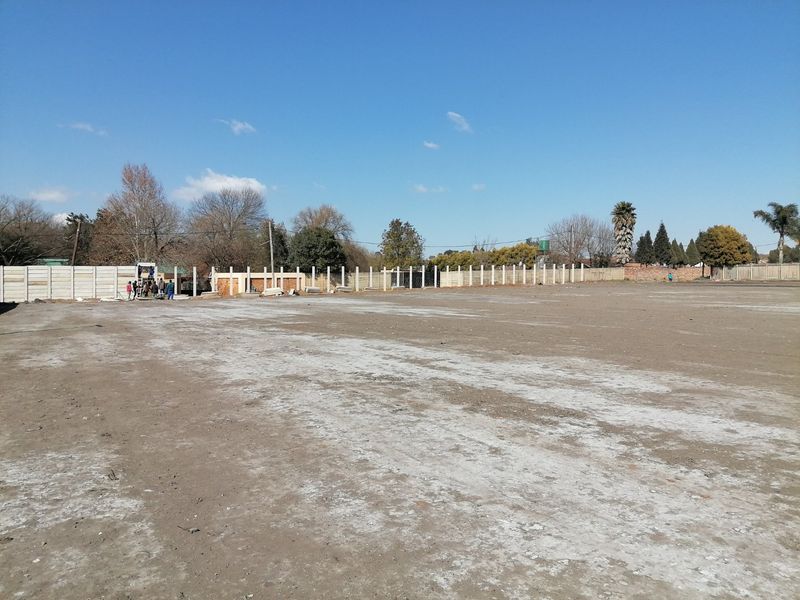 A large, cleared residential vacant land plot featuring a perimeter precast concrete boundary wall under a clear blue sky.