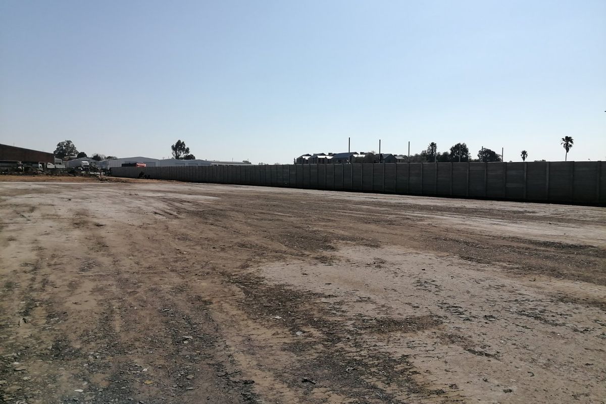 A vacant residential land plot featuring a long precast concrete boundary wall and an open, unpaved ground surface.