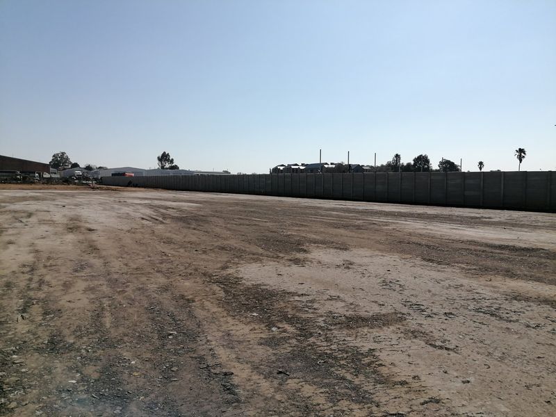 A vacant residential land plot featuring a long precast concrete boundary wall and an open, unpaved ground surface.