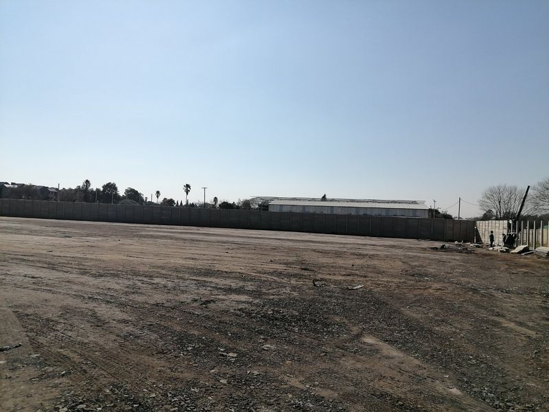 A large, vacant residential plot featuring a perimeter precast concrete boundary wall, offering a blank canvas for future development.