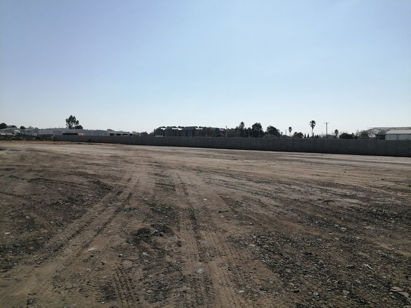 A wide, vacant residential plot featuring cleared earth and a perimeter boundary wall, offering a blank canvas for future development.