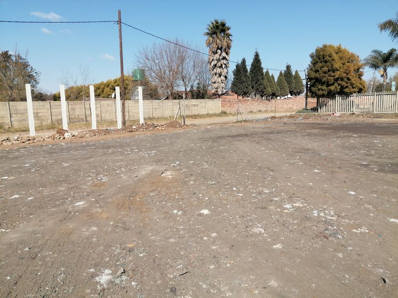 A vacant residential plot featuring a level dirt surface, perimeter precast concrete walling, and existing fence posts.