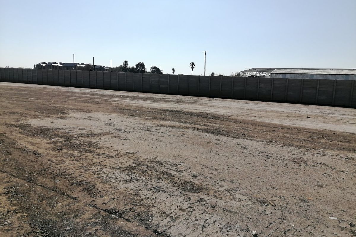 A large, vacant residential plot featuring a precast concrete boundary wall and an unimproved dirt surface, ready for development.