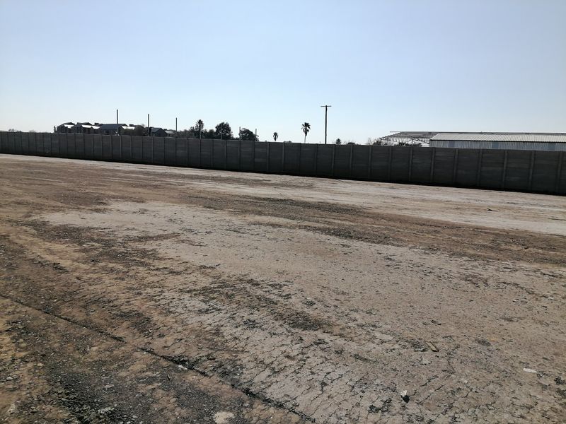 A large, vacant residential plot featuring a precast concrete boundary wall and an unimproved dirt surface, ready for development.