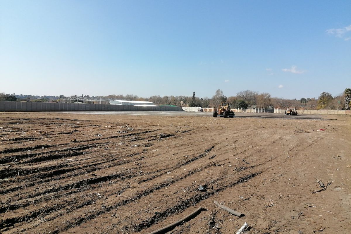 A large, cleared residential vacant land plot featuring a perimeter precast concrete boundary wall and ongoing site preparation work.